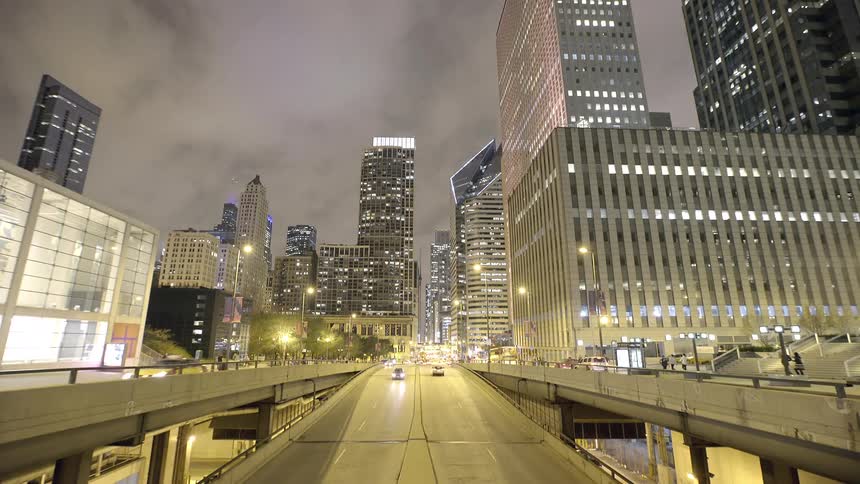 A wide shot captures the flow of traffic on a city highway at night, surrounded by the glow of illuminated downtown skyscrapers