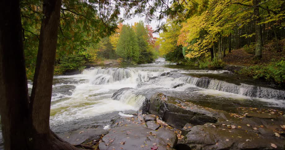 A picturesque waterfall rushes over stone ledges in a forest bursting with vibrant autumn colors