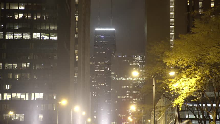 An iconic skyscraper is framed between two modern buildings on a foggy night in downtown Chicago