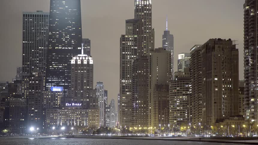 The iconic Chicago skyline glows at night as traffic creates light streaks along the waterfront of Lake Michigan