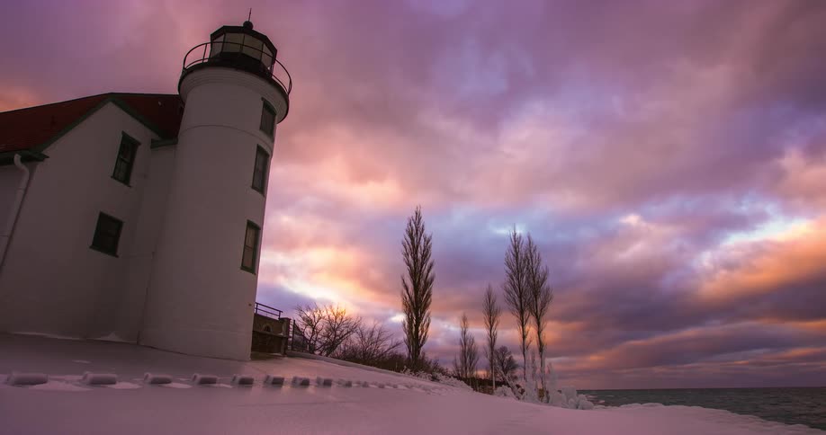 Stunning timelapse of a snowy lighthouse on a winter shore with a vibrant purple and pink sky at dusk