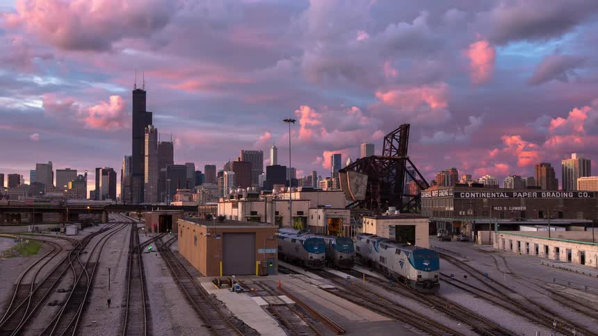 A stunning timelapse of a vibrant sunset over the Chicago skyline with train tracks and industrial buildings in the foreground