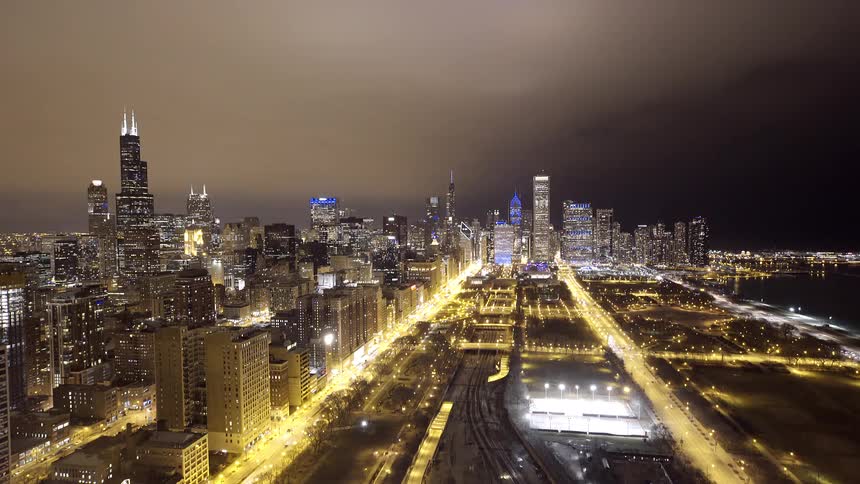 A high-angle time-lapse captures the vibrant Chicago skyline at night, with glowing skyscrapers and streaks of traffic