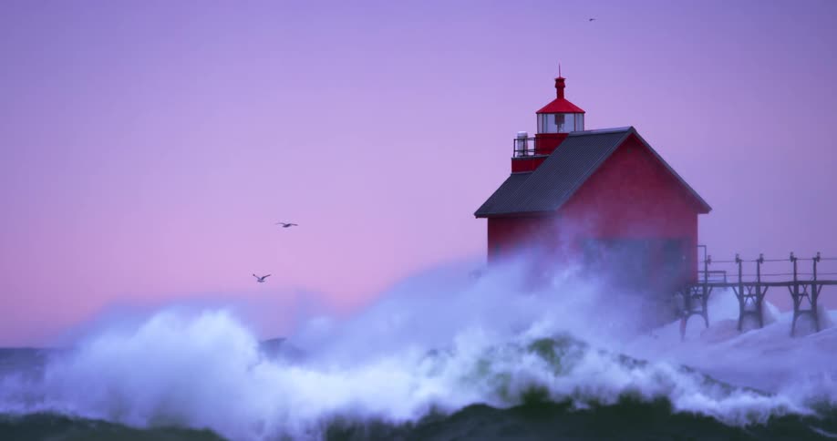 In stunning slow motion, powerful waves crash against a vibrant red lighthouse on a frozen pier during a stormy twilight