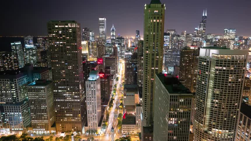An elevated time-lapse view captures the vibrant energy of downtown Chicago at night as traffic streaks down the canyon of illuminated skyscrapers