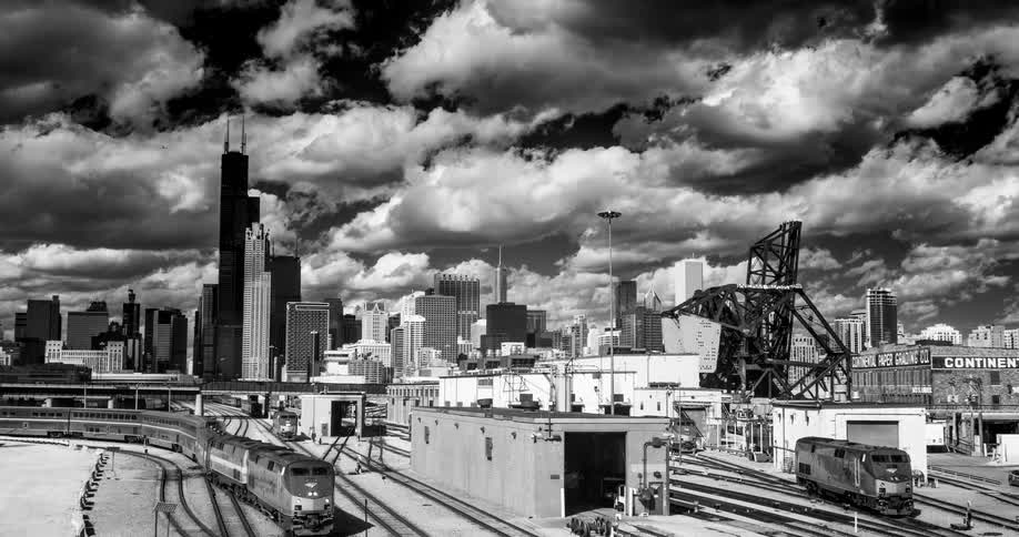 Black and white cinemagraph of a train arriving in a Chicago rail yard against the city skyline and a dramatic sky