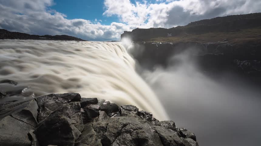 A long-exposure time-lapse captures the immense power of Iceland's Dettifoss waterfall, with silky water cascading into a misty canyon under moving clouds