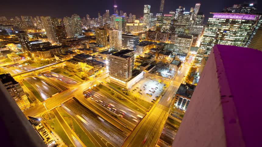 A vibrant time-lapse from a rooftop showcases the illuminated Chicago skyline and streaks of light from traffic on the busy highways below at night