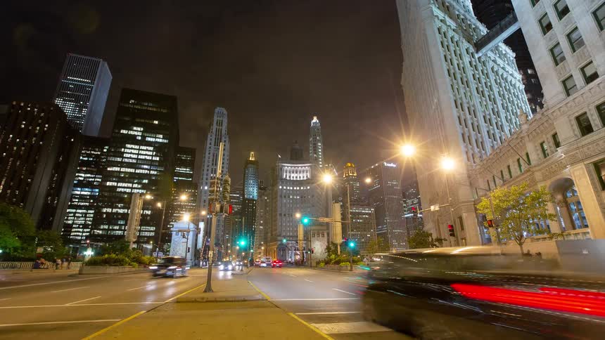 Low-angle time-lapse captures the vibrant energy of a downtown city intersection at night as traffic streaks by illuminated skyscrapers