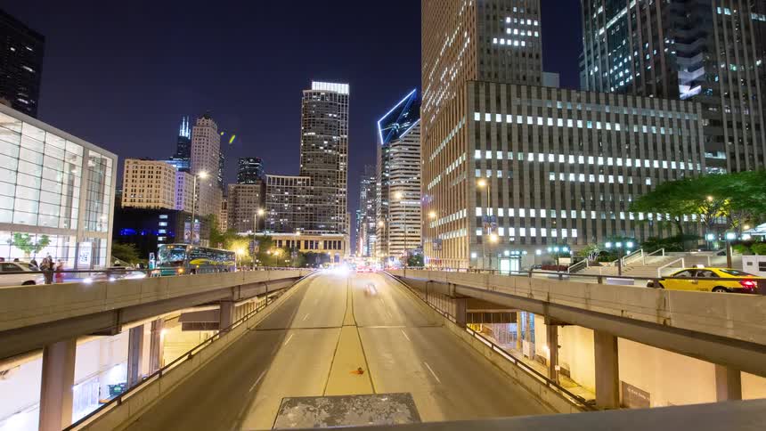 A dynamic timelapse reveals the bustling Chicago cityscape at night, with traffic creating vibrant light trails on the multi-level highway below