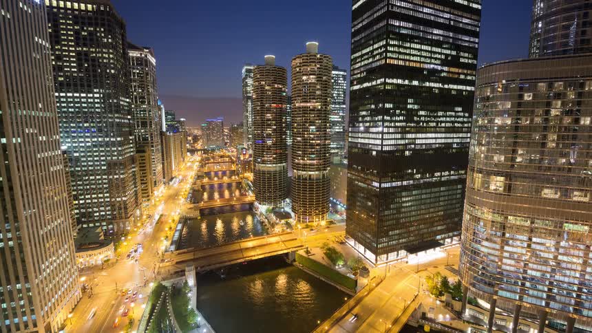 Elevated time-lapse view of the iconic Chicago River and Wacker Drive as dusk turns into a vibrant night, with city lights reflecting in the water