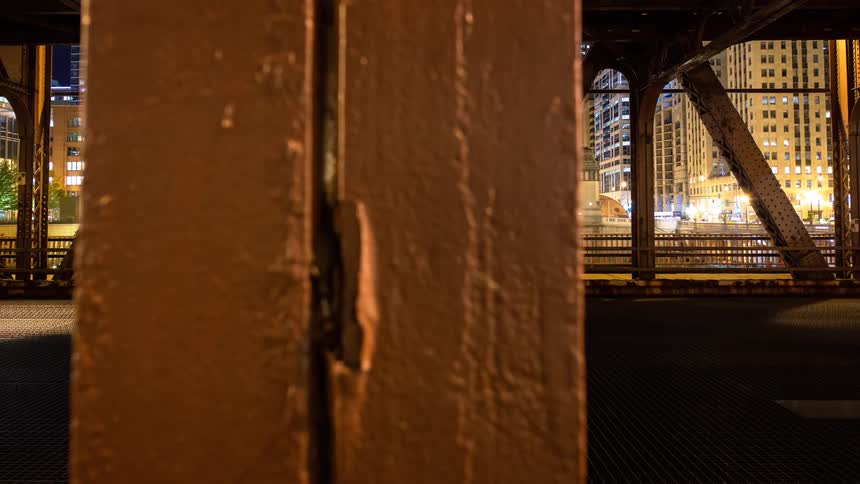 A dynamic dolly timelapse captures the bustling Chicago city traffic and skyline at night from within the industrial steel structure of a bridge