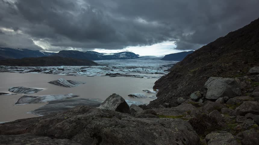 Storm clouds roll over a vast glacier and its lagoon filled with icebergs in a dramatic Icelandic landscape time-lapse