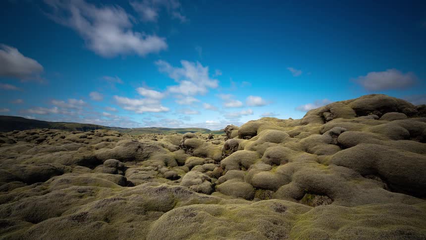 A stunning timelapse captures clouds moving across a vibrant blue sky over Iceland's surreal, green, moss-covered lava fields