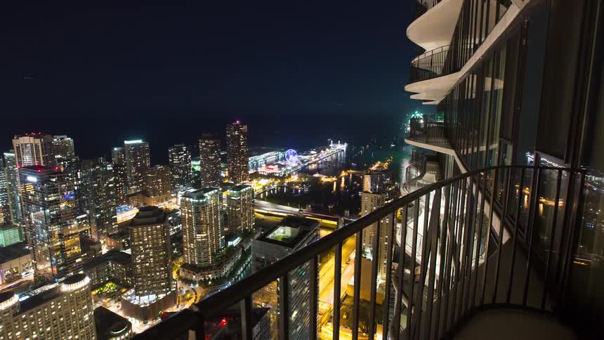 A sweeping night time-lapse from a high-rise balcony shows the Chicago skyline, Navy Pier, and celebratory fireworks over Lake Michigan