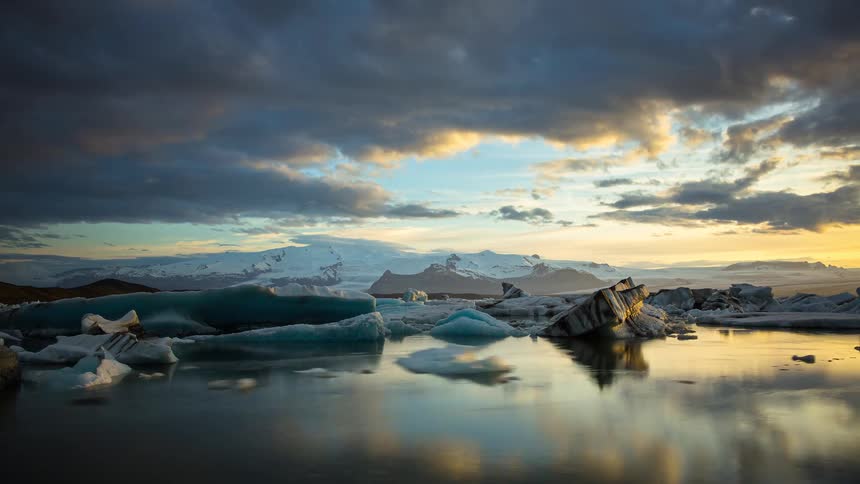 Stunning timelapse of icebergs drifting through a glacial lagoon in Iceland as a golden sunset breaks through dramatic clouds