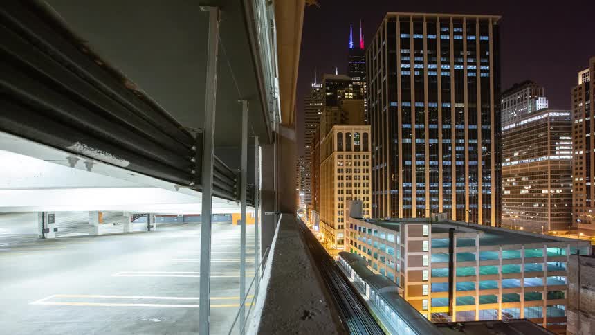 A time-lapse dolly shot reveals the Chicago city skyline at night from a parking garage as an elevated train passes below