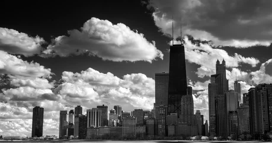 A dramatic black and white time-lapse shows clouds moving over the iconic Chicago skyline and the John Hancock Center