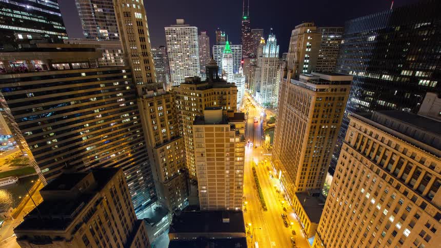 An epic high-angle timelapse captures the vibrant energy of a downtown cityscape at night, with traffic creating luminous light trails below
