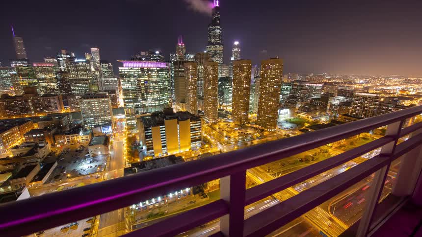 A dynamic time-lapse reveals the bustling Chicago skyline and glowing expressways at night from a high-rise balcony
