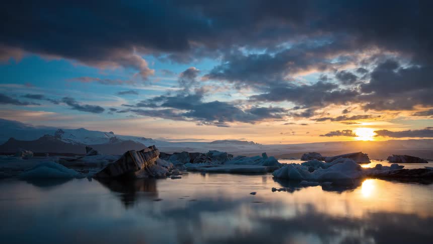 A breathtaking time-lapse captures a dramatic sunset over an Icelandic glacial lagoon, where icebergs float as clouds paint the sky