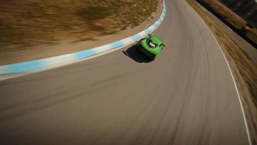 An FPV drone captures a dynamic aerial view of a green sports car racing around a tight curve on a track