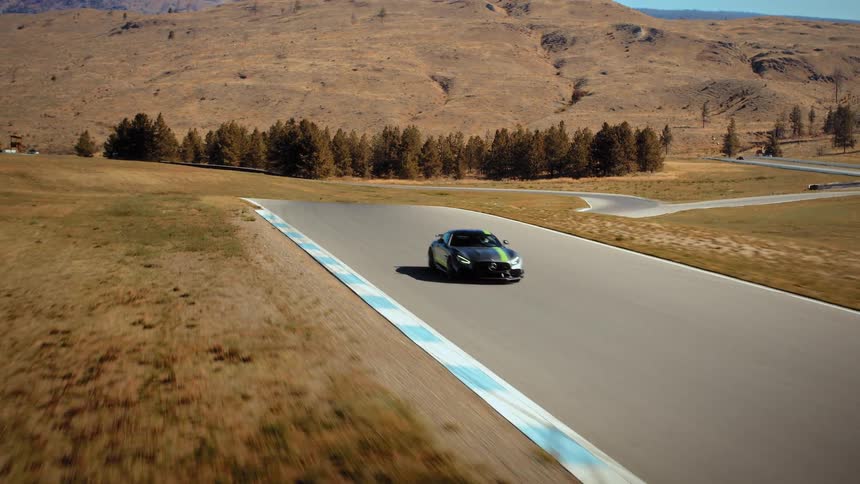 An aerial view tracks a fast-moving luxury sports car as it expertly navigates a racetrack surrounded by dry hills