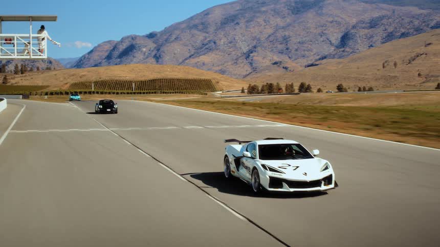 A sleek white sports car completes a lap on a professional racetrack, passing the finish line in a scenic, mountainous landscape