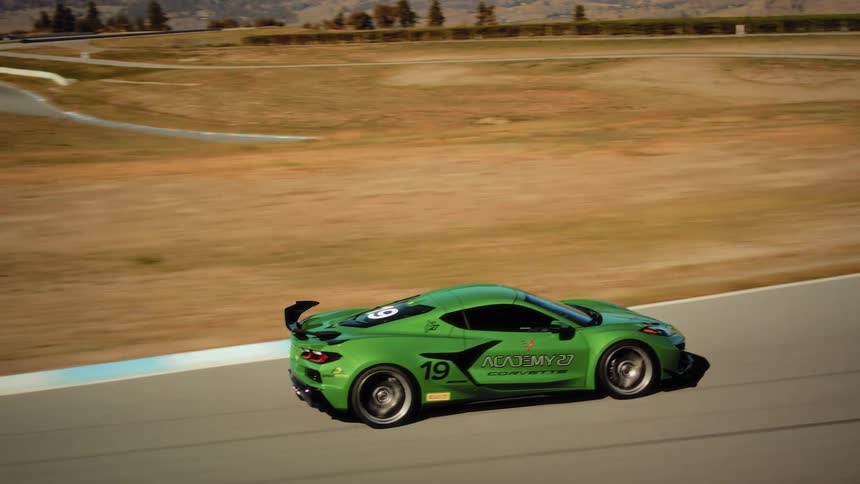 A lime green Corvette race car comes into focus while driving down a straightaway and into a corner on a professional racetrack in slow motion