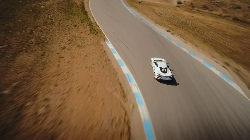 An exhilarating aerial pursuit follows a white high-performance sports car as it speeds around a winding race track in the mountains