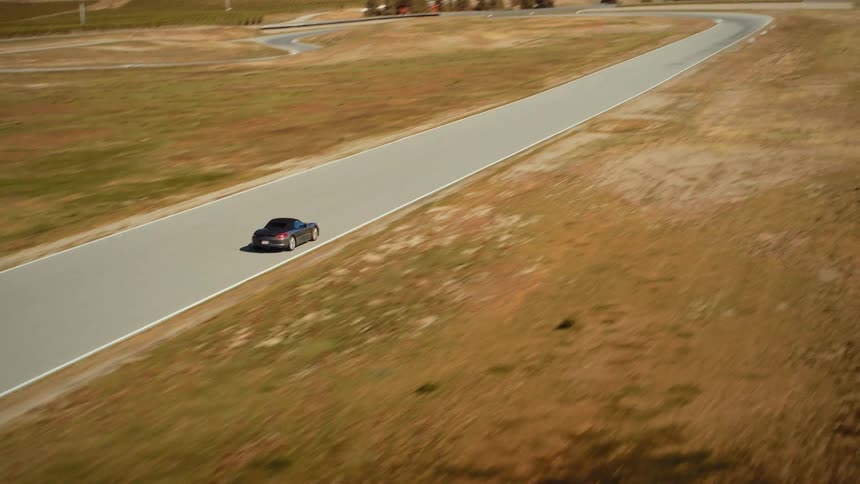 An aerial view of a sleek grey convertible sports car driving along a winding racetrack in a vast, arid mountain landscape