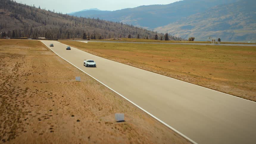 Dynamic aerial footage follows a white supercar as it accelerates down a straightaway on a desert race track