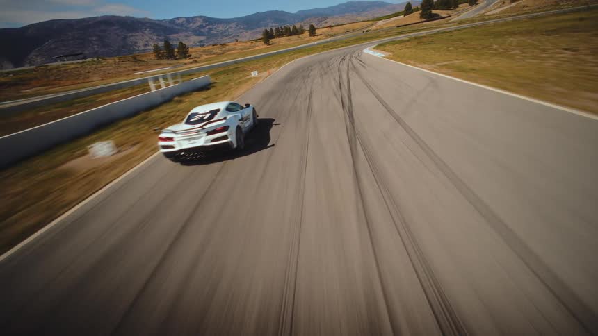 Dynamic aerial drone footage follows a white Corvette sports car as it expertly navigates the turns of a professional race track at high speed