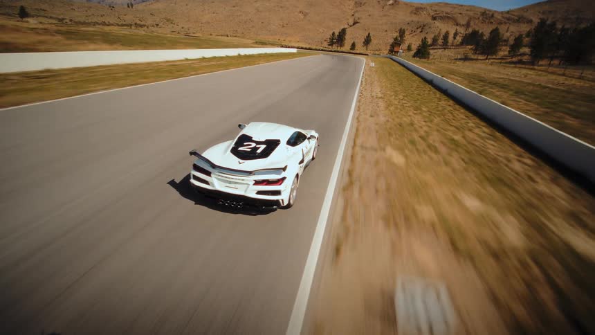 Dynamic aerial chase shot following a white number 21 sports car as it speeds along a racetrack through a dry, sunny landscape