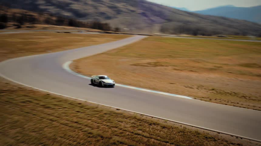 Aerial tracking shot of a white sports car speeding around a turn on a scenic racetrack in an arid, hilly landscape