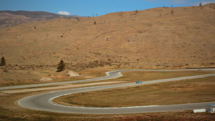 A panning shot reveals a winding racetrack where several sports cars race through an arid, hilly landscape