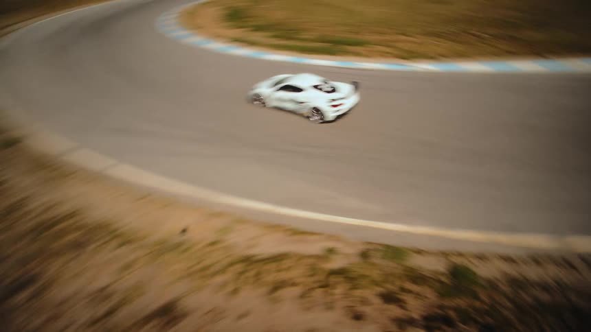 Thrilling FPV drone footage tracks a white sports car as it speeds around a corner on a professional racetrack