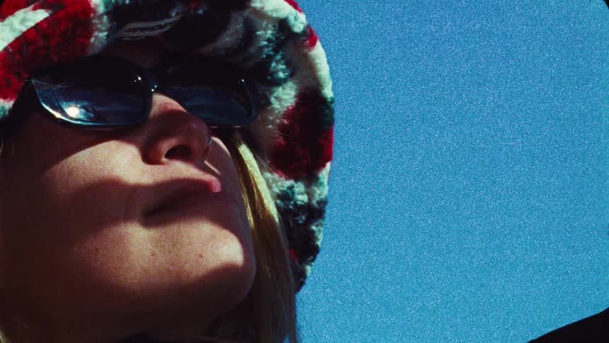 Vintage film close-up of a cool young woman in a fuzzy bucket hat and sunglasses basking in the sun against a clear blue sky
