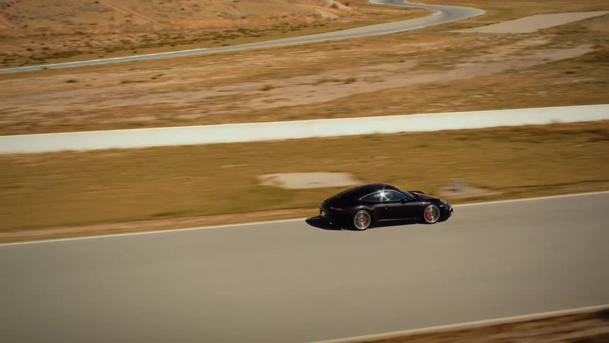 A sleek black sports car speeds along a professional race track through a dry, arid landscape on a sunny day