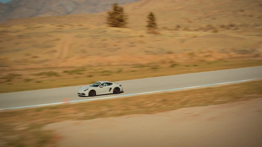 A sleek white sports car speeds along a winding racetrack set in a vast, arid desert landscape