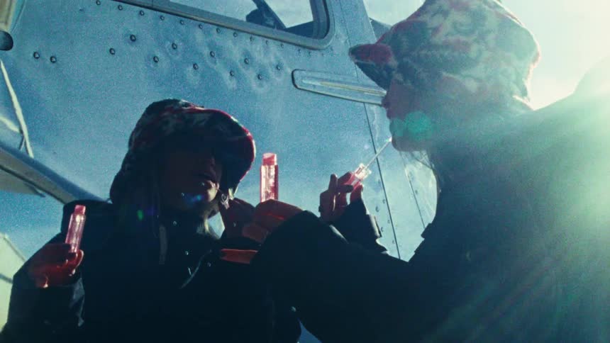 A low-angle, vintage-style shot shows two women in winter hats applying lipstick next to a silver Airstream trailer