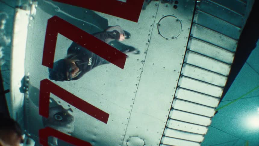The reflection of a vintage pilot in a flight suit is seen on the riveted metal wing of a historical aircraft