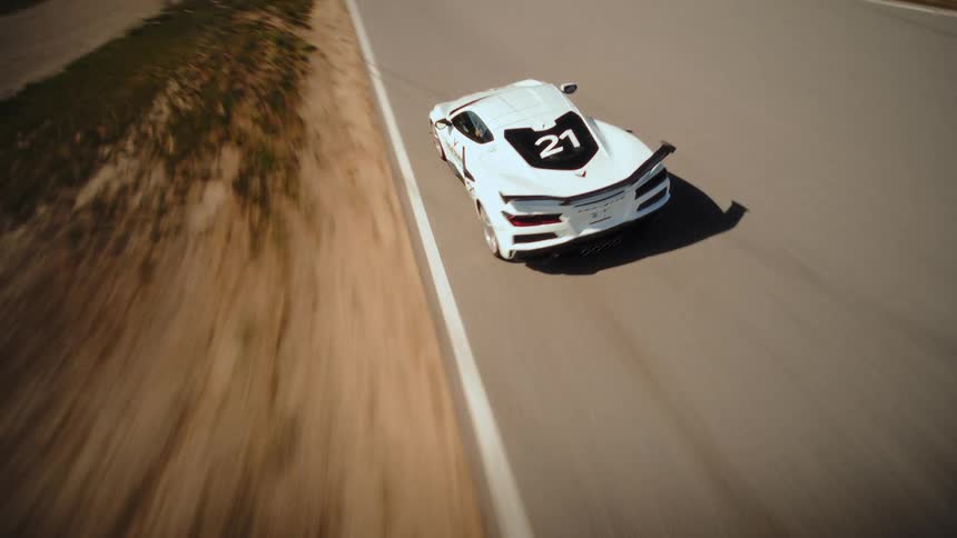 An FPV drone captures a thrilling high-speed pursuit of a white Corvette sports car as it skillfully navigates the curves of a race track