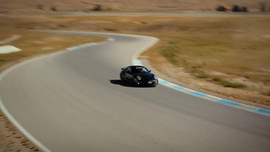 A sleek black sports car speeds around a tight curve on a professional racetrack in a desert environment