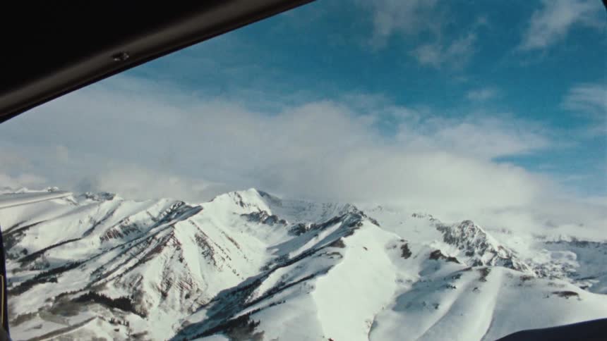 An aerial point-of-view shot from a plane window flying over a majestic, snow-covered mountain range on a clear day