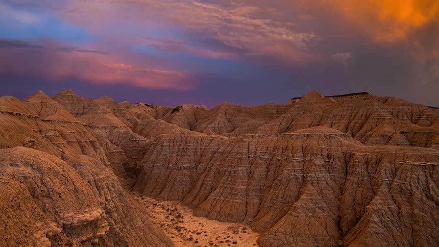 A dramatic timelapse captures a vibrant sunset fading into a deep twilight sky over the rugged and eroded Badlands landscape