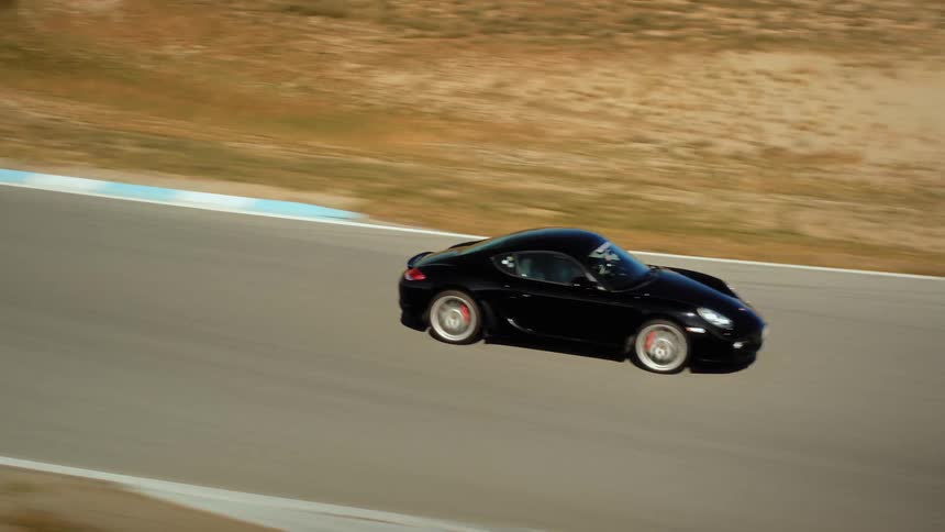 An exciting aerial view follows a black sports car leading two others around a race track in a beautiful, arid mountain landscape