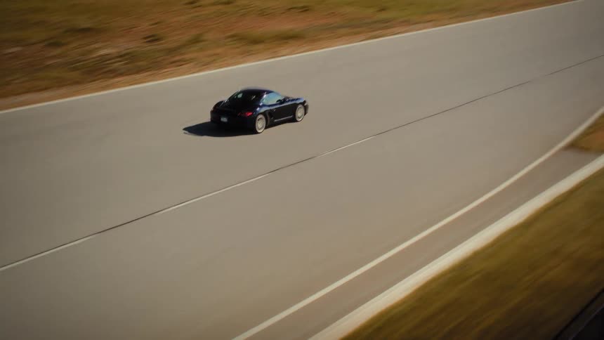High-angle aerial shot follows a black luxury sports car as it drives at speed on a professional race track