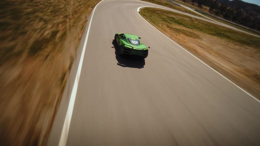 An exhilarating FPV drone shot chases a lime green supercar as it speeds around the winding curves of a professional racetrack