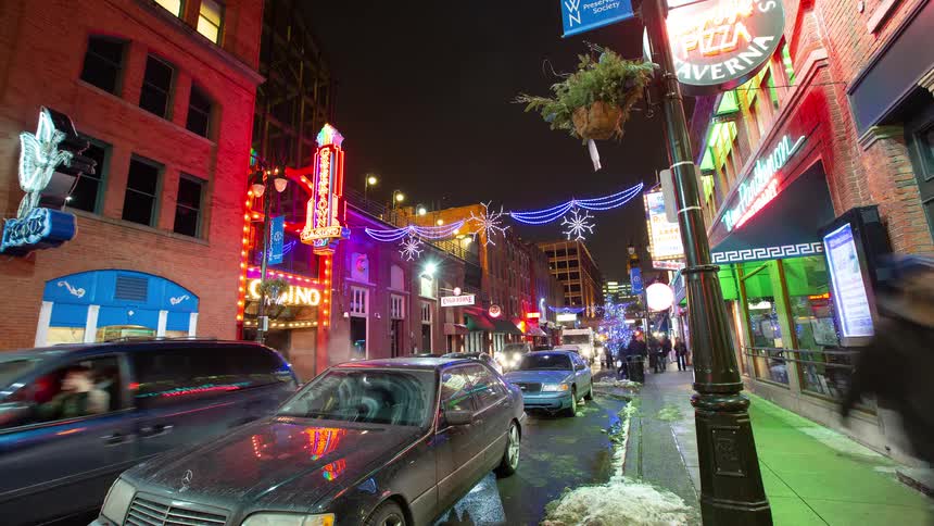 A vibrant time-lapse of a city entertainment district at night with neon signs, holiday lights, and bustling traffic